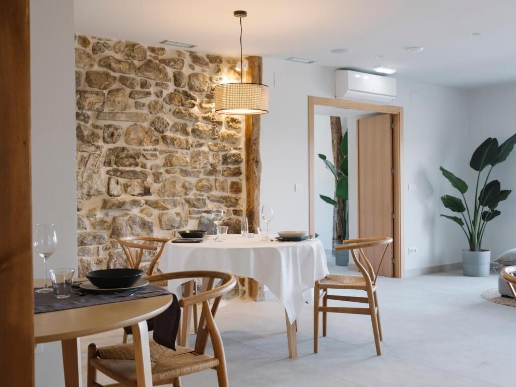 A dining area with a stone wall, wooden chairs, a white tablecloth-covered table, and a hanging light fixture.