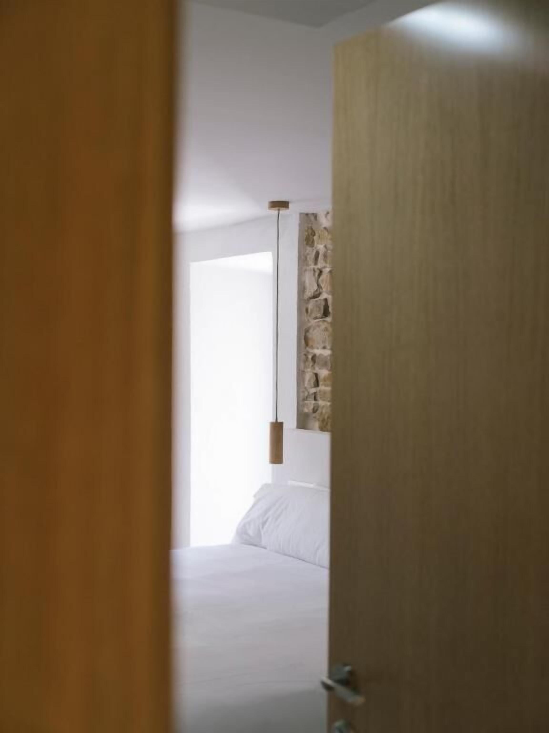 Un dormitorio con una pared de acento de piedra, una lámpara colgante y una cama con ropa de cama blanca.