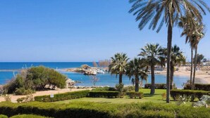 A coastal landscape with palm trees, a beach, and boats. - Beachfront apartmen located just a stone's throw away from Ayia Triada beach (Paralimni)