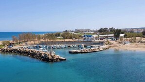 A marina with boats docked, a rocky breakwater, and buildings in the background. - Beachfront apartmen located just a stone's throw away from Ayia Triada beach (Paralimni)