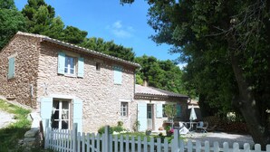 A stone house with a white picket fence, a patio with outdoor furniture, and a tree providing shade. - Charming 3-bedroom home with a private pool at the foot of Mont Ventoux. Stunning view (Bédoin)