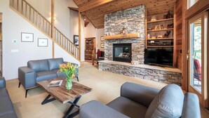 Un salon moderne avec une cheminée en pierre, des canapés gris, une table basse en bois et un escalier avec des rampes en bois.