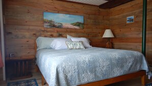 A wooden cabin-style bedroom with a bed, pillows, a painting on the wall, and a lamp. - Beautiful sunsets and relaxing days, are waiting for you at Harborside  Cottage. (Tremont)