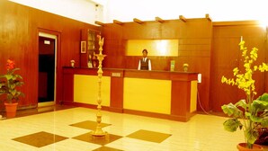 A reception area with a wooden reception desk, a decorative pillar, and potted plants. - Hotel Coastal Residency (Namakkal)