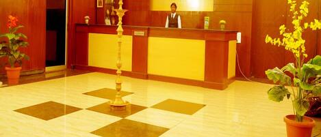 A reception area with a wooden reception desk, a decorative pillar, and potted plants.