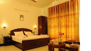 A well-lit bedroom with a bed, a nightstand, a wardrobe, a glass table, and a chair. - Hotel Coastal Residency (Namakkal)