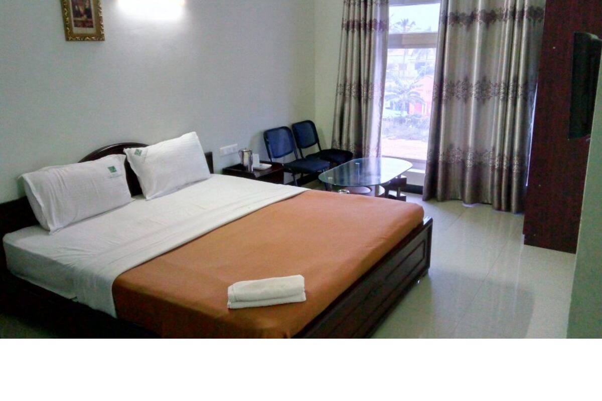 Una habitación de hotel con cama, una mesita, dos sillas y una ventana con cortinas.