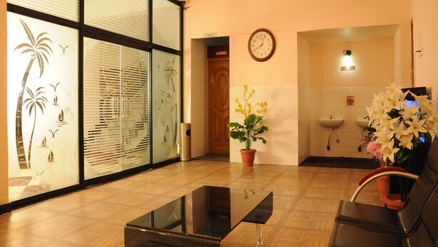 A reception area with a glass partition, a clock, a potted plant, a sink, and a seating area with chairs. - Hotel Coastal Residency (Namakkal)