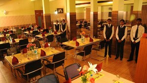 A dining area with multiple tables set for service, each with a waiter standing by. - Hotel Coastal Residency (Namakkal)