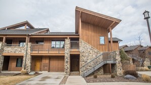 Une maison à deux étages avec une façade en pierre, une terrasse en bois et un escalier d’entrée.
