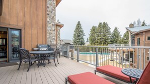 Une terrasse en bois avec des meubles d’extérieur, un barbecue et une vue sur une piscine et des arbres.