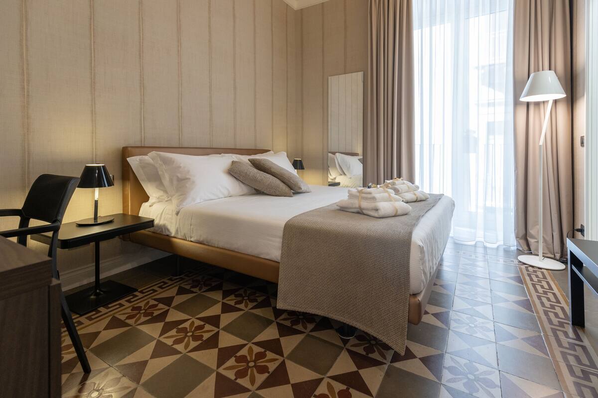 Ein Hotelzimmer mit Bett, Nachttischen, einem Schreibtisch und einem gemusterten Boden.