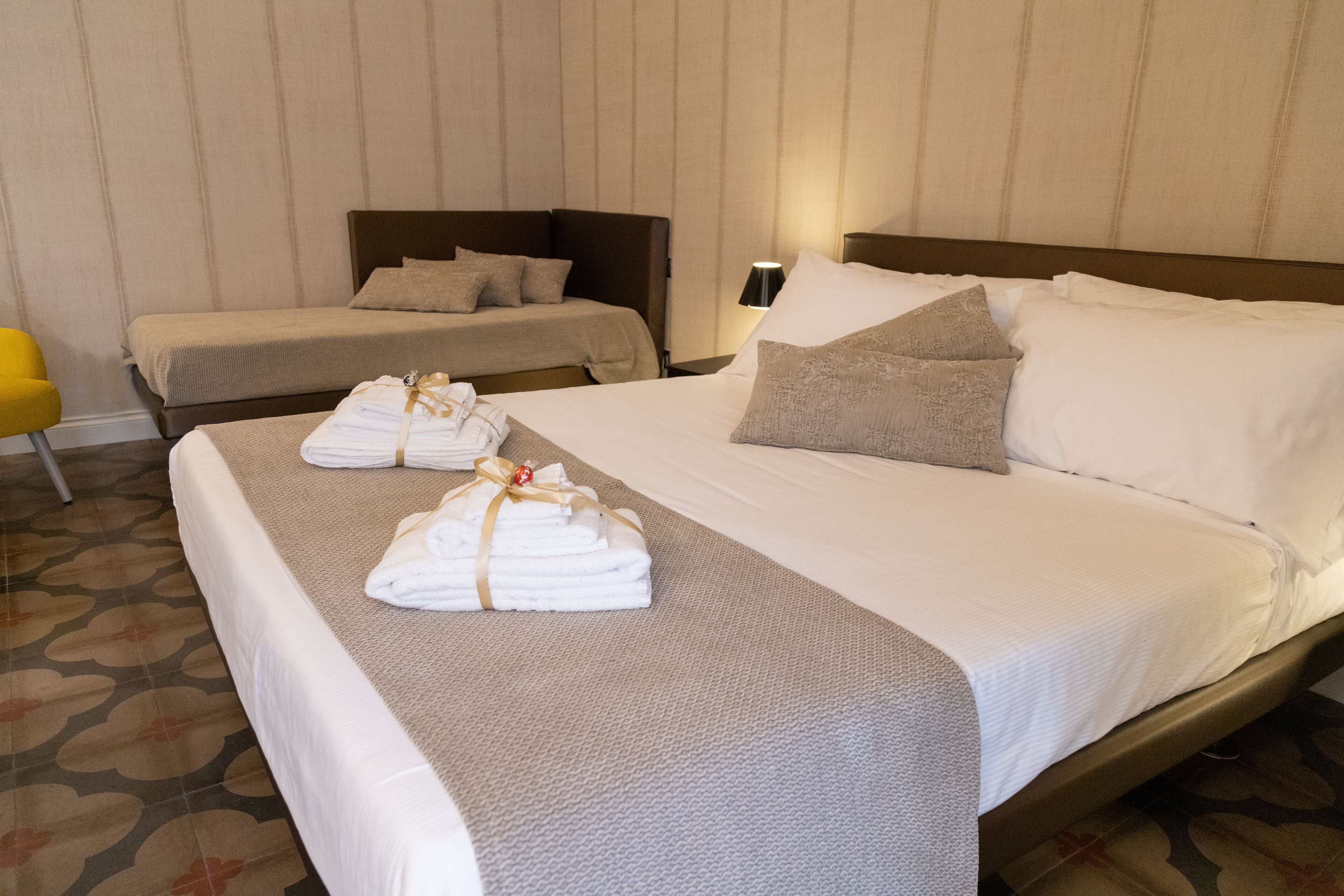 Habitación de hotel con dos camas, una mesita de noche, una lámpara y una silla amarilla.