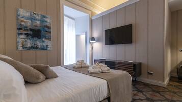 A hotel room with a large bed, a flat-screen TV mounted on the wall, a bedside table with a lamp, and a painting on the wall.