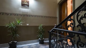 A hotel lobby with a checkered floor, two potted plants, a decorative border, and a sign above a wooden door.