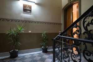 Un vestíbulo de hotel con piso a cuadros, dos plantas en macetas, un borde decorativo y un letrero sobre una puerta de madera.
