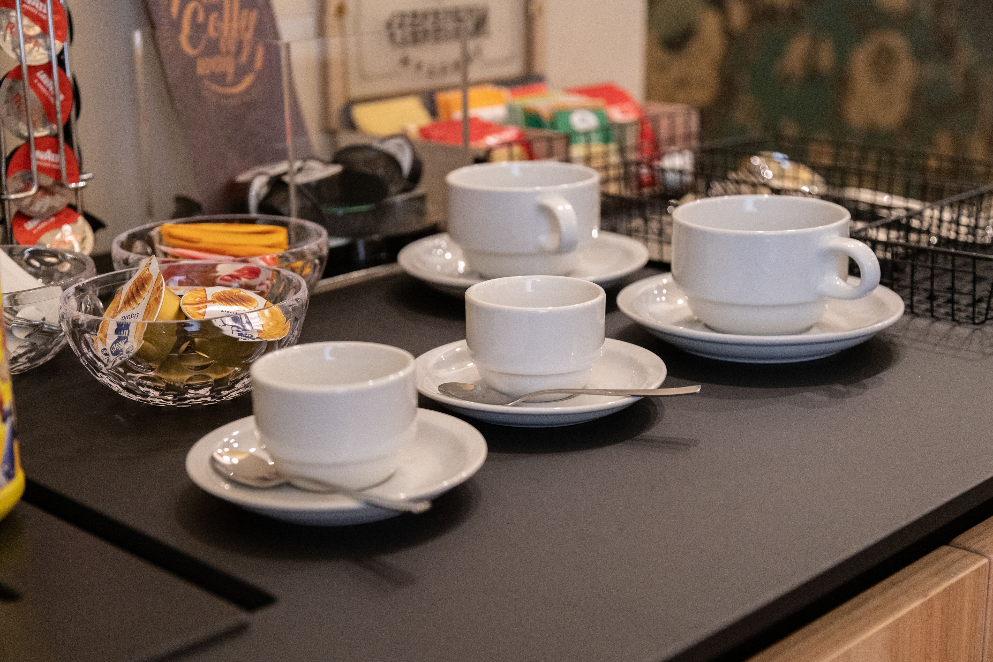 A table with white cups and saucers, a spoon, and a glass bowl containing a snack.