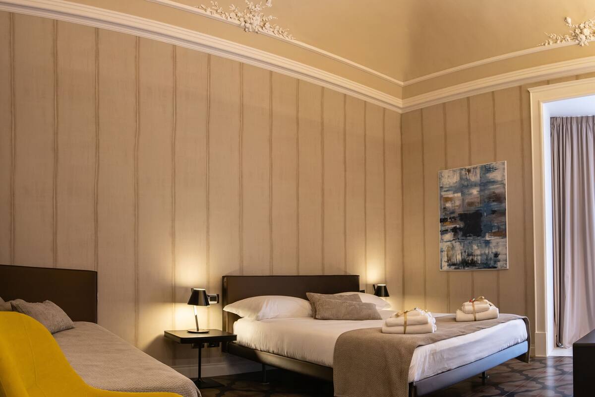 Ein Hotelzimmer mit einem großen Bett, einem gelben Sessel, einem Bild an der Wand und einer dekorativen Decke.