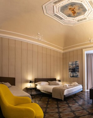 Habitación de hotel con una cama grande, un sillón amarillo, un cuadro en la pared y un techo decorativo.