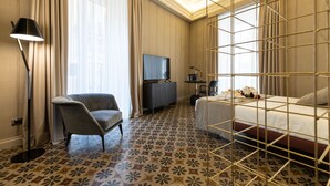Habitación de hotel con cama, escritorio, silla, televisor y piso con estampado floral.
