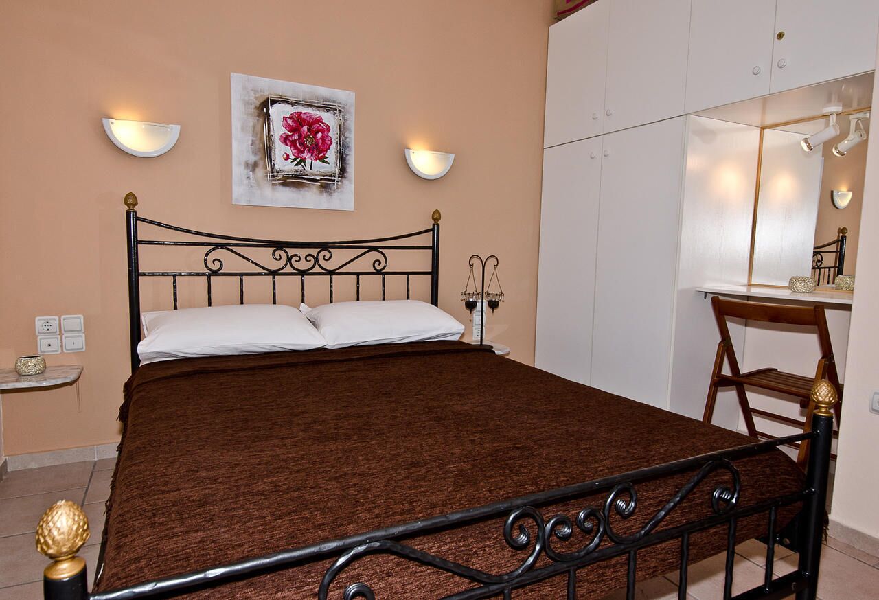 Un lit bien fait, recouvert d’une couverture marron, une table de chevet avec une lampe et un luminaire fixé au mur.