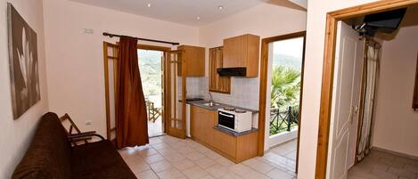 Un espacio habitable compacto con kitchenette, sofá y puerta corredera que da a un área exterior.