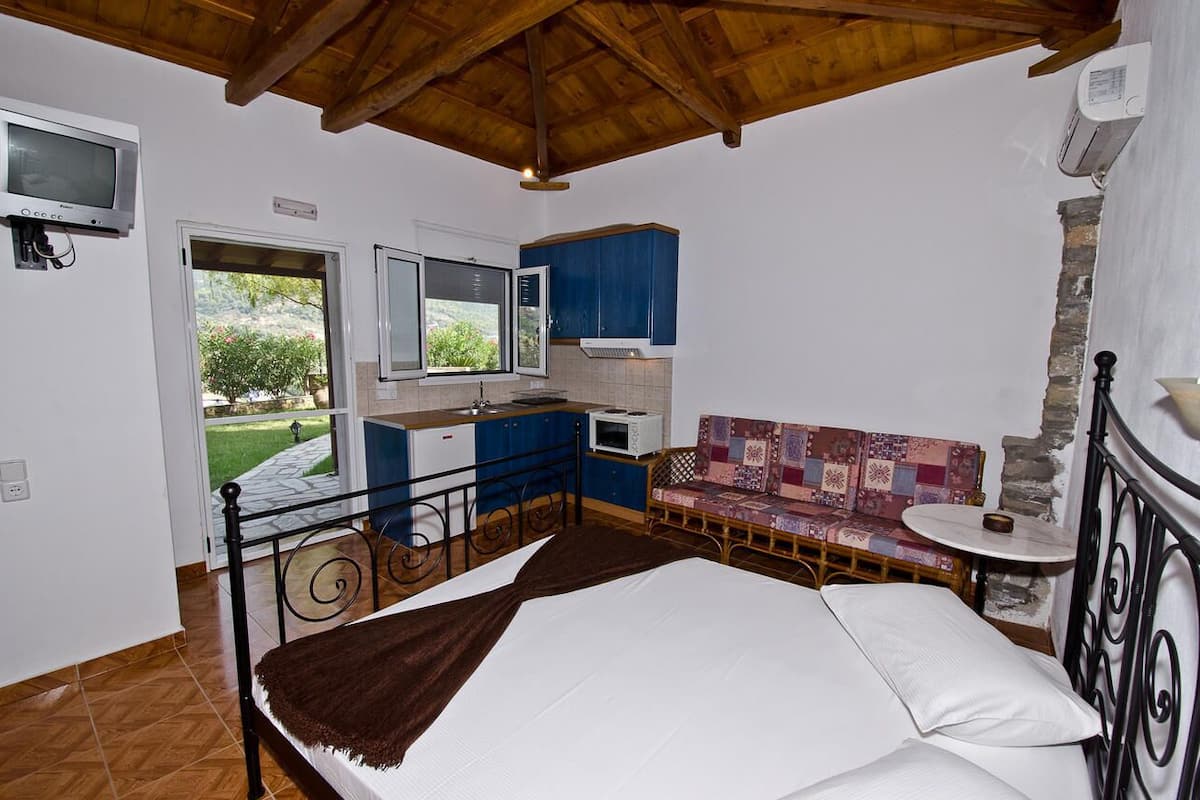 A bedroom with a bed, a small kitchenette, a window, and a view of greenery.