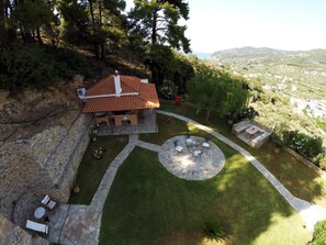 A house with a stone exterior, a tiled roof, and a circular patio area with outdoor furniture. - Likasti (Skopelos)