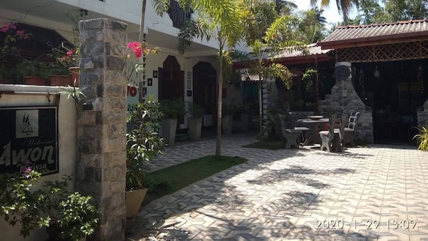 A courtyard with a stone pathway, potted plants, a small outdoor seating area, and a building with a balcony. - AWON Hotel (Mirissa)