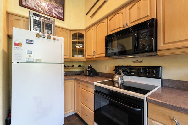 A kitchen with wooden cabinets, a white refrigerator, a black microwave, a stove, and a kettle.