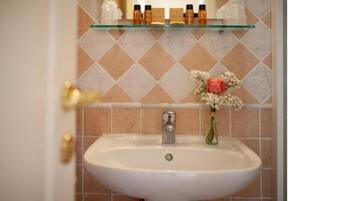 Un baño con un lavamanos blanco, un estante de vidrio arriba y un jarrón decorativo con flores.