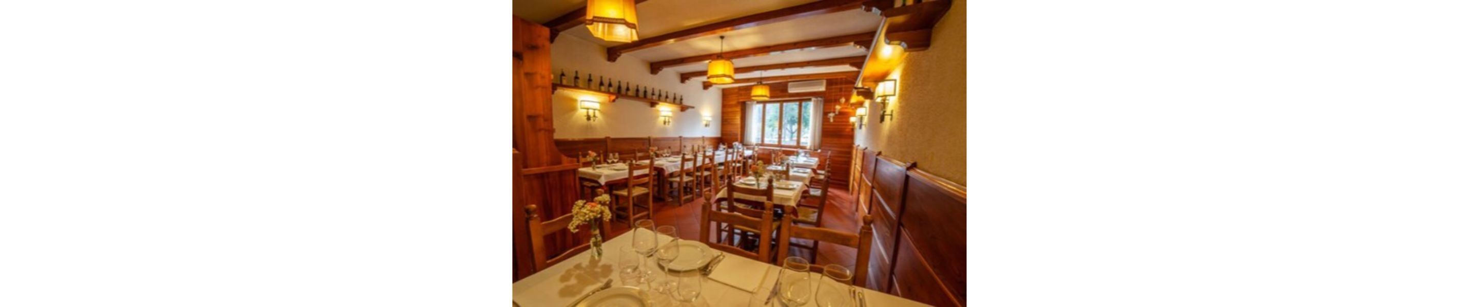 A restaurant interior with wooden tables and chairs, warm lighting, and a view of the outdoors through a window.