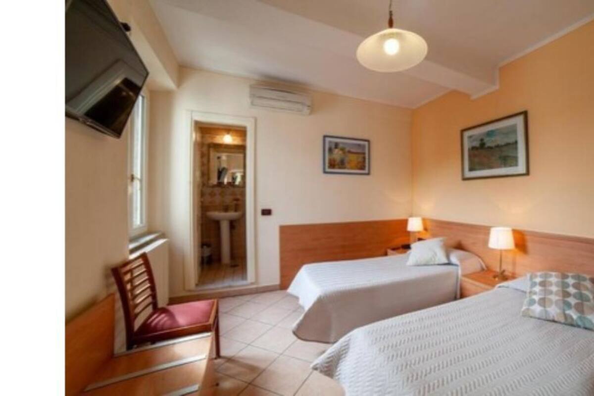 A hotel room with two beds, a wooden chair, a TV mounted on the wall, and a door leading to another room.
