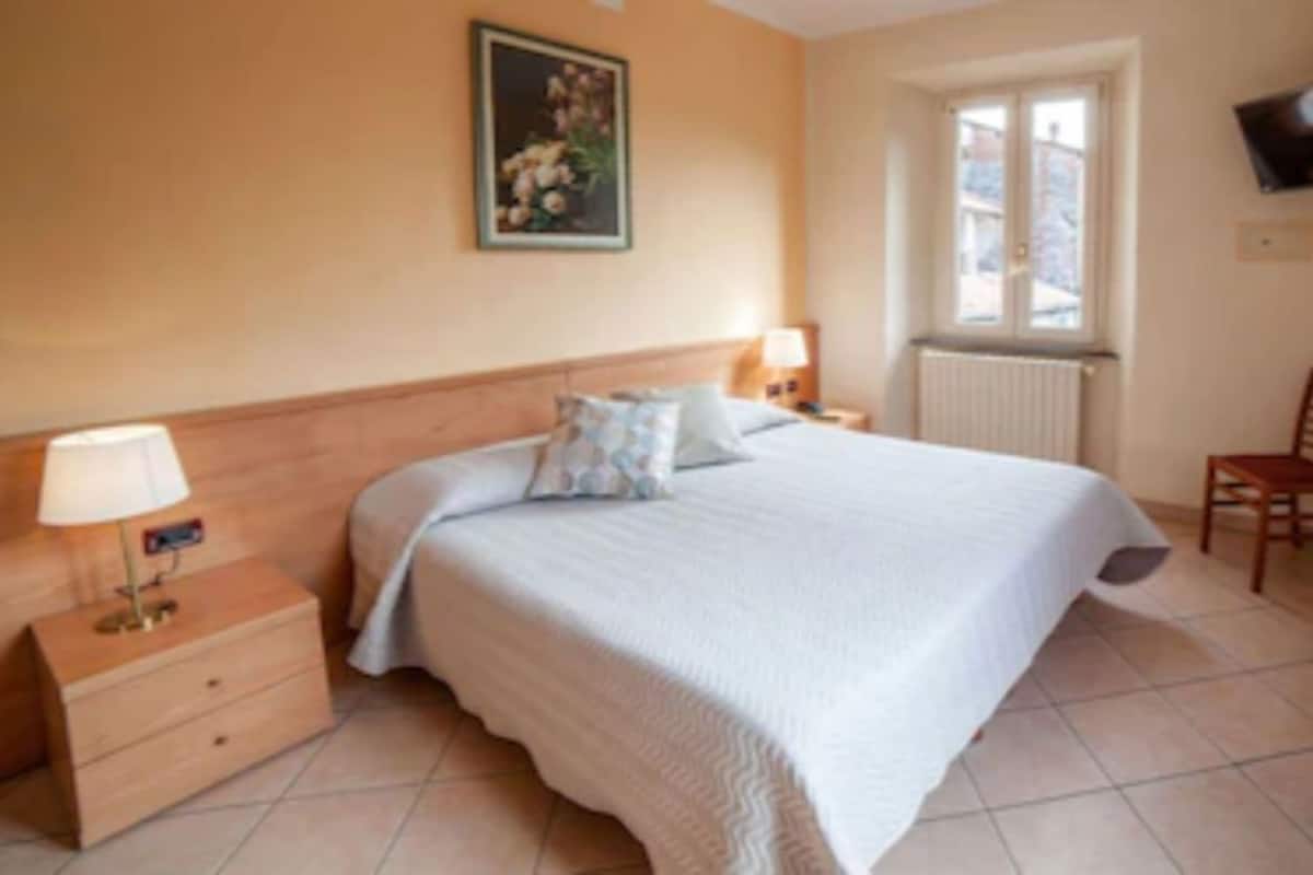 A bedroom with a bed, bedside table, lamp, chair, and a window.
