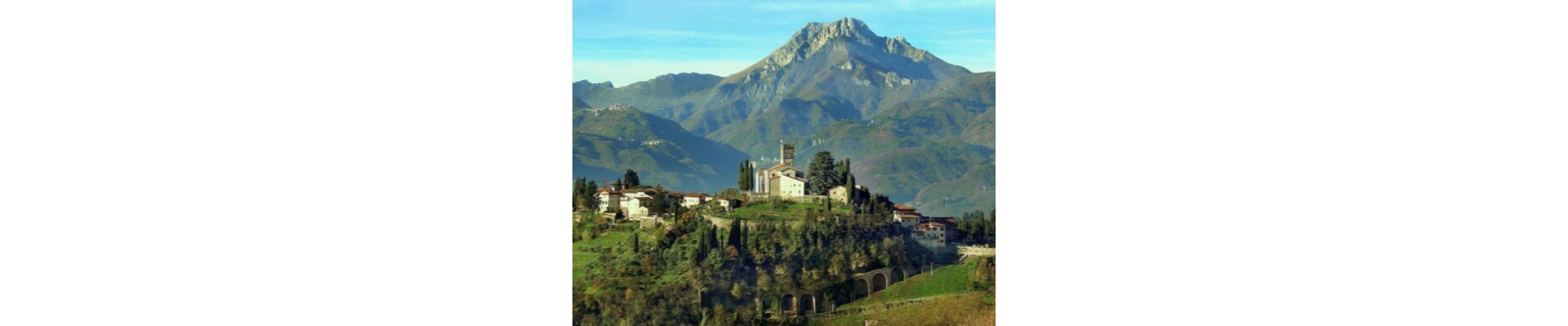 A mountain village with a church on a hill, surrounded by lush greenery and a prominent mountain in the background.