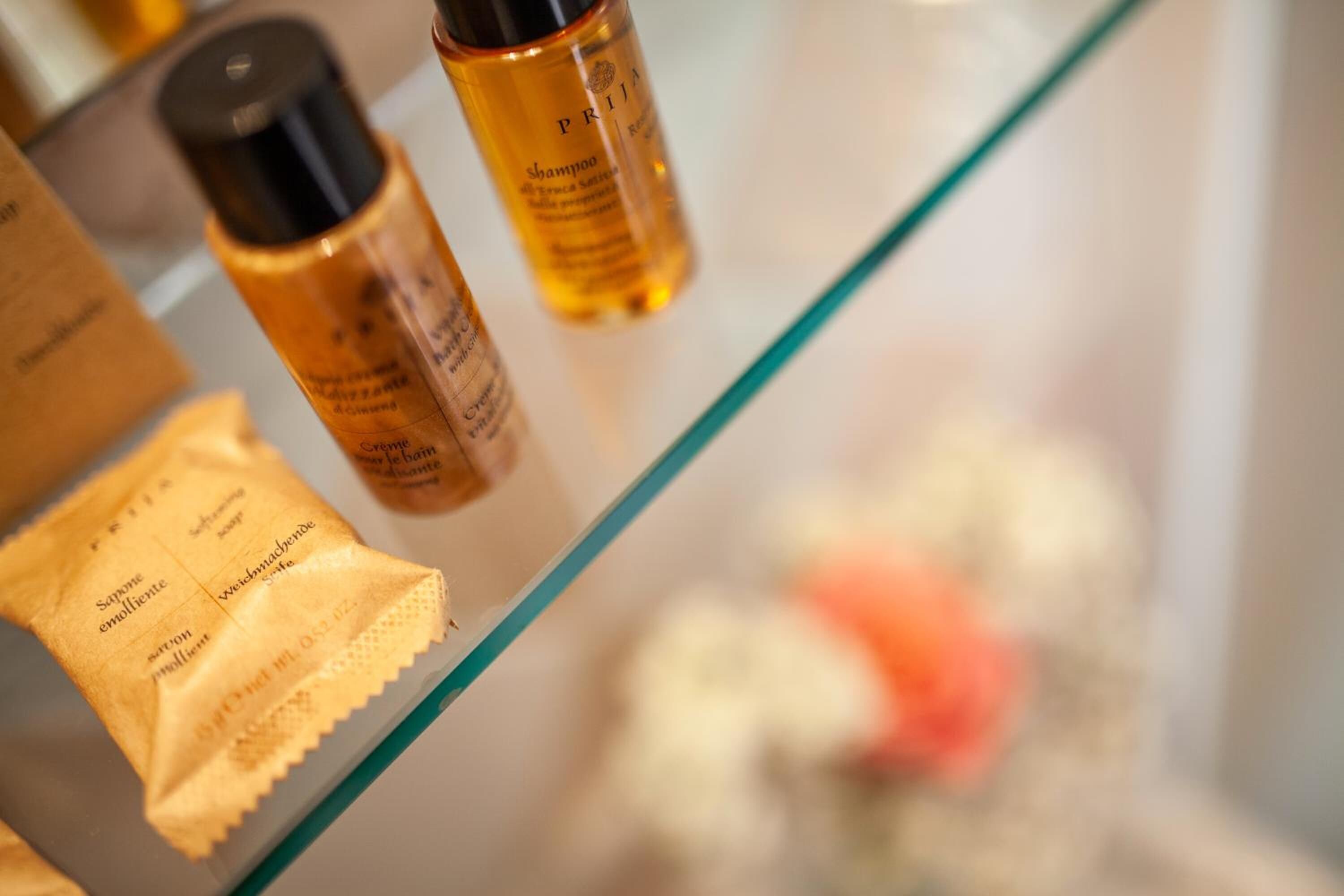 A bathroom shelf with toiletries including a shampoo bottle, a soap bar, and a packet of soap.