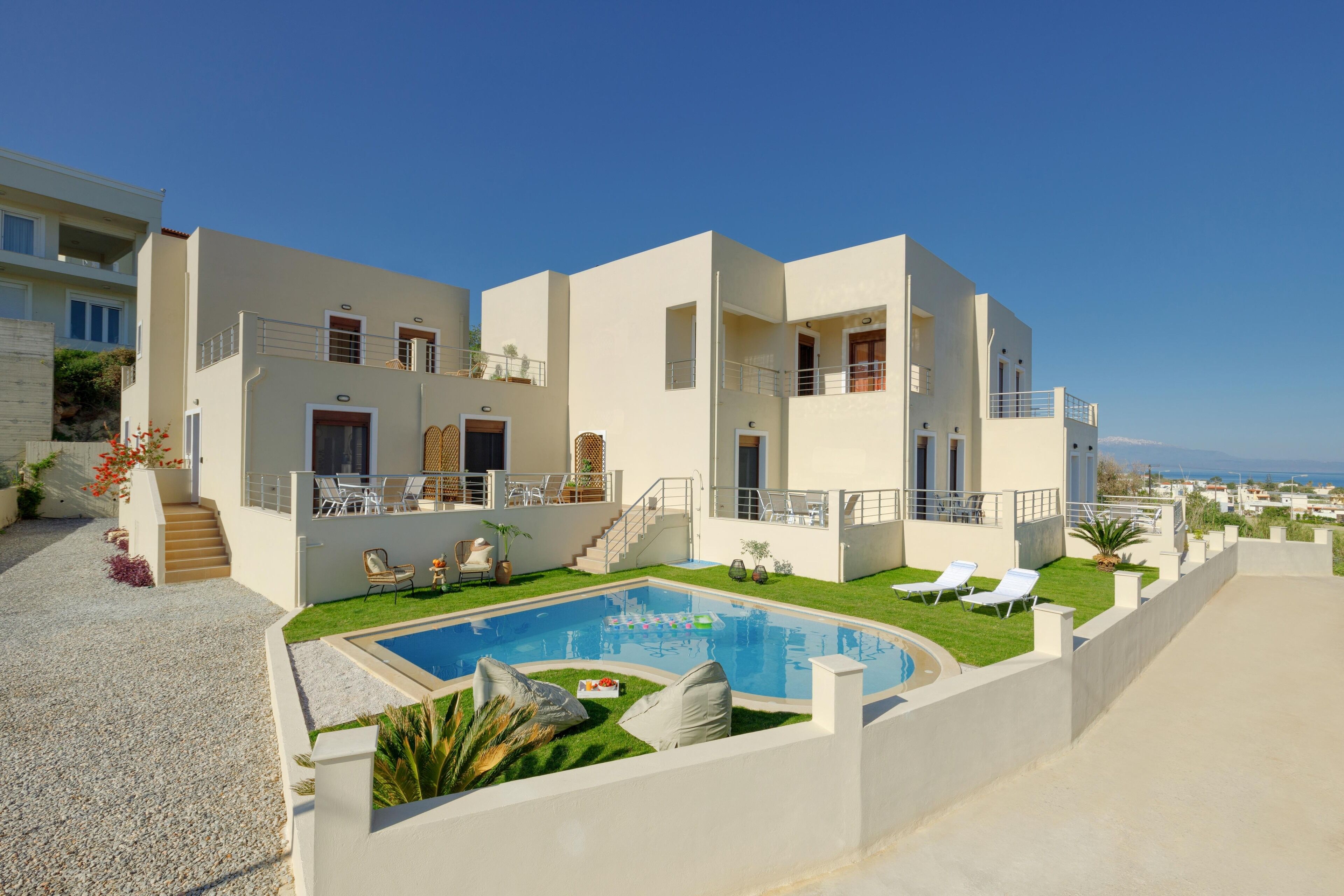 A modern two-story house with a swimming pool, outdoor seating, and a view of the sea.