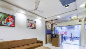 A modern hotel lobby with a brown sofa, a small wooden table, ceiling fans, and artwork on the walls. - ABS Hotel (Noida)