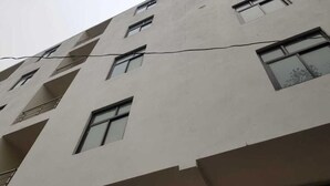 A multi-story building with a flat facade, multiple windows, and a visible power line. - ABS Hotel (Noida)