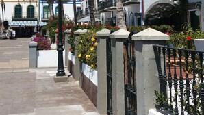 A coastal street with white buildings, palm trees, and a clear blue sky.