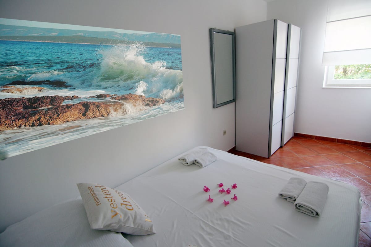 A hotel room with a bed, a painting of the sea, a wardrobe, and a window.