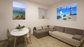 A living room with a white round table, two chairs, a brown sectional sofa, and two wall-mounted pictures depicting coastal scenes. - Villa Rajski Dvor1 (Bol)