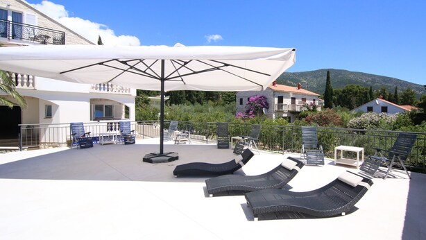 A rooftop terrace with lounge chairs, a large umbrella, and a view of the surrounding landscape. - Villa Rajski Dvor1 (Bol)