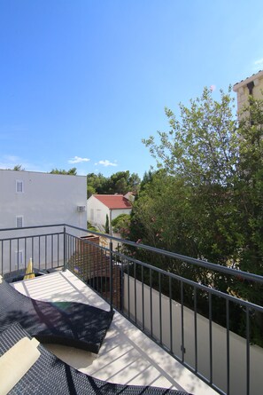 Ein Balkon mit Metallgeländer, einer weißen Wand und einem Gebäude mit rotem Dach im Hintergrund.