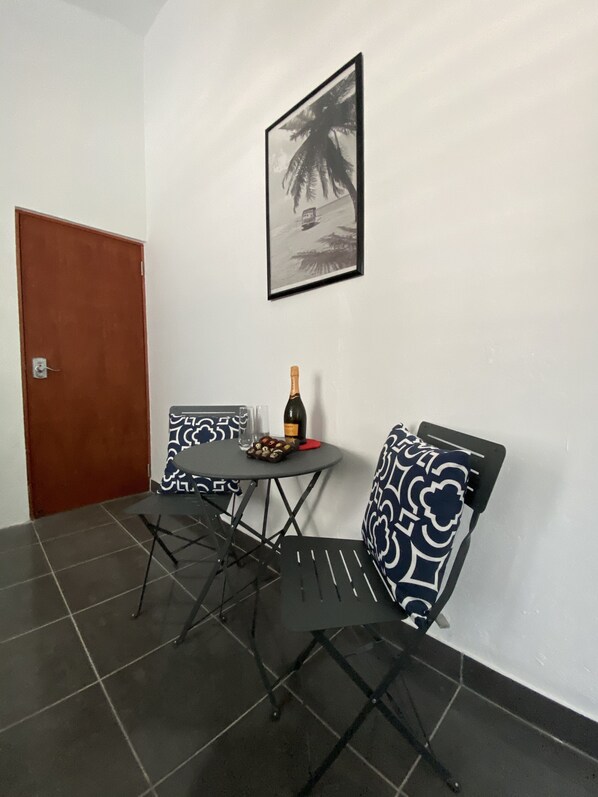 A small dining area with a table, chairs, a bottle of wine, and a framed picture on the wall.