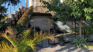 A stone building with a tiled roof, a staircase, and a garden with various plants. - Les Gîtes de L'Aven - la Forestiere (Orgnac L'aven)