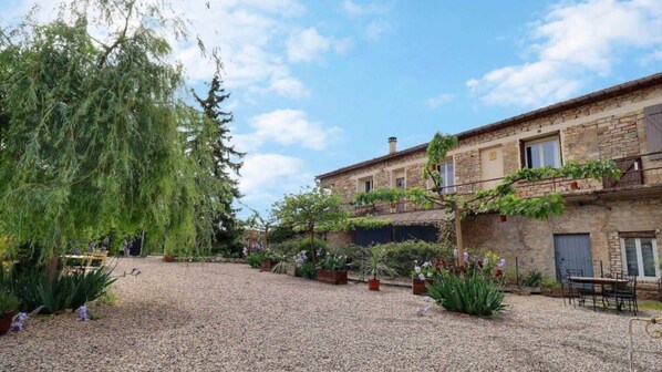 A courtyard with a gravel ground, surrounded by stone buildings with balconies and potted plants.
