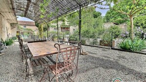 An outdoor patio with a wooden table and metal chairs, surrounded by gravel and greenery. - Les Gîtes de L'Aven - la Forestiere (Orgnac L'aven)