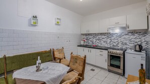 Eine kompakte Küche mit weißen Schränken, einer Marmor-Spritzschutzwand, einem Herd, einer Kaffeemaschine und einem kleinen Kühlschrank.
