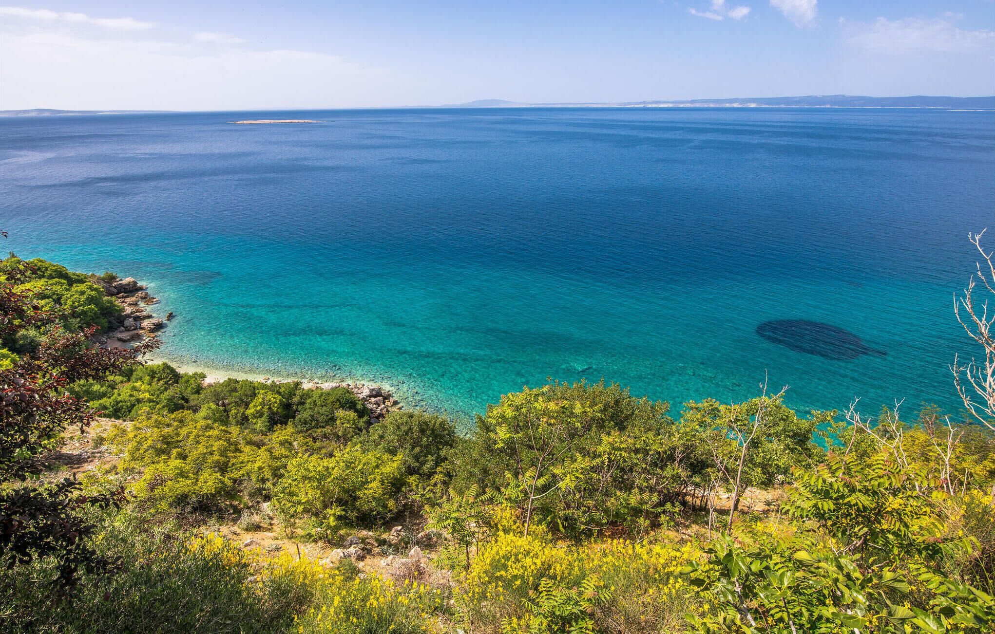 Un paysage côtier caractérisé par une eau turquoise cristalline, une côte rocheuse et une végétation verdoyante et luxuriante.